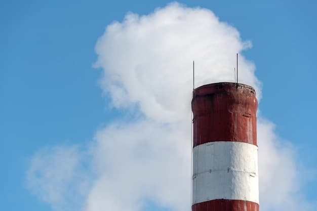 An industrial building and a chimney with white smoke against a blue sky Air pollution from the smoke of a working factory Chemical industry and the risk of environmental disaster